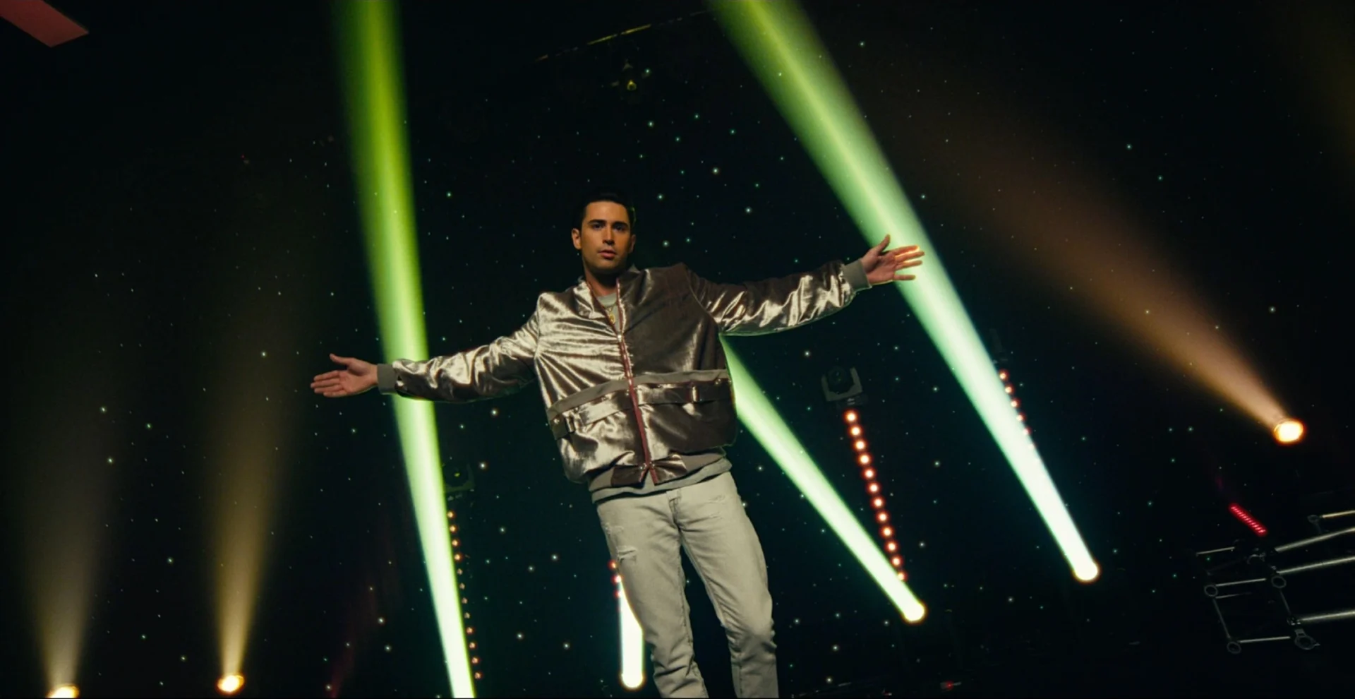 A man in silver jacket standing on stage with lights.